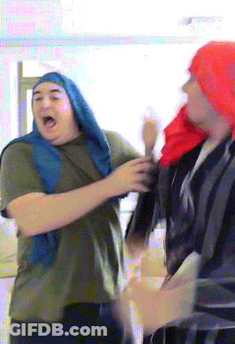 A Man Wearing A Red Hat And A Blue Scarf Stands Next To Another Man GIF
