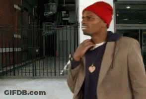 A Man Wearing A Red Hat And A Brown Jacket Is Standing In Front Of A Building GIF