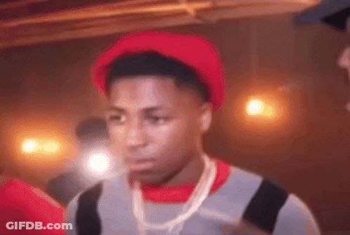 A Man Wearing A Red Hat And A Necklace Is Standing In A Dark Room . GIF