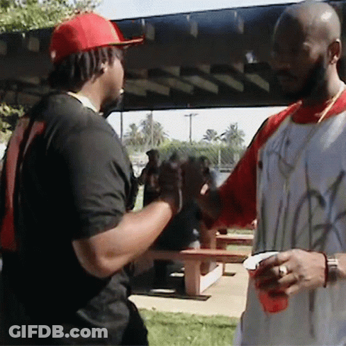 A Man Wearing A Red Hat Is Shaking Hands With Another Man Wearing A White Shirt With Graffiti On It GIF