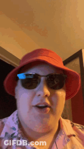 A Man Wearing A Red Hat , Sunglasses And A Pink Shirt Is Making A Funny Face . GIF