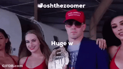 A Man Wearing A Red Hat That Says Make America Great Again Is Holding A Championship Trophy Surrounded By Three Women . GIF