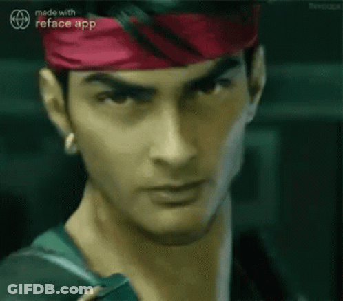 A Man Wearing A Red Headband And A Green Jacket Is Looking At The Camera . GIF