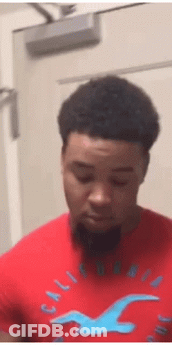 A Man Wearing A Red Hollister Shirt With A Blue Bird On It Is Standing In Front Of A Door . GIF
