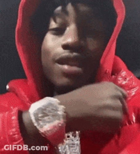 A Man Wearing A Red Hoodie And A Watch Is Looking At The Camera . GIF
