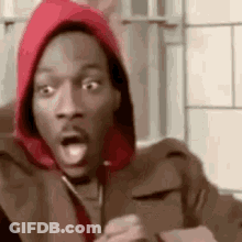 A Man Wearing A Red Hoodie Is Making A Surprised Face While Holding A Cell Phone . GIF