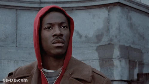 A Man Wearing A Red Hoodie Is Standing In Front Of A Building GIF