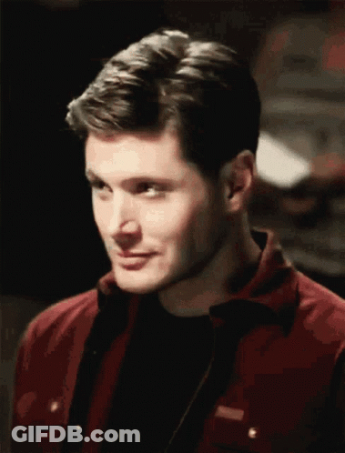 A Man Wearing A Red Jacket And A Black Shirt Is Smiling GIF