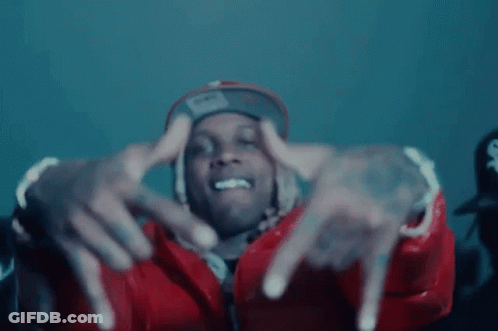 A Man Wearing A Red Jacket And A Hat Is Making A Hand Gesture . GIF