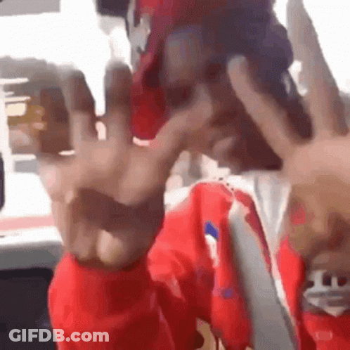 A Man Wearing A Red Jacket And A Red Hat Is Making A Peace Sign With His Hands . GIF