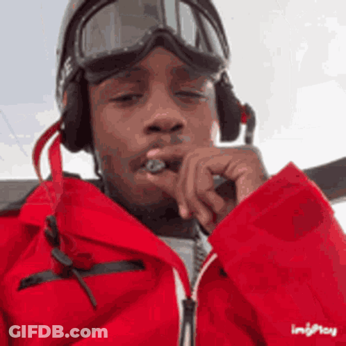 A Man Wearing A Red Jacket , Goggles And Headphones Is Smoking A Cigarette . GIF