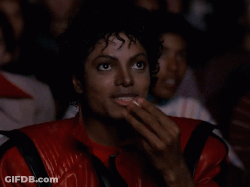 A Man Wearing A Red Jacket Is Eating Popcorn GIF