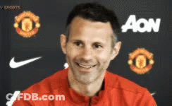 A Man Wearing A Red Jacket Is Smiling In Front Of An Aon Banner GIF