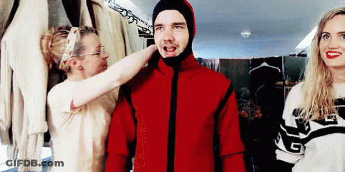 A Man Wearing A Red Jacket With A Hood Is Being Helped By Two Women . GIF