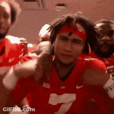 A Man Wearing A Red Jersey And A Headband Is Standing In Front Of A Group Of People . GIF