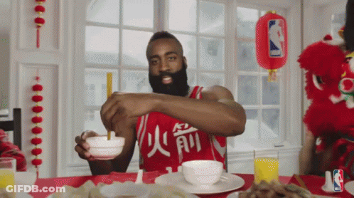 A Man Wearing A Red Jersey With Chinese Characters On It Sits At A Table With Bowls Of Food GIF