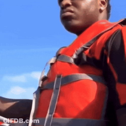 A Man Wearing A Red Life Jacket Is Holding A Steering Wheel GIF