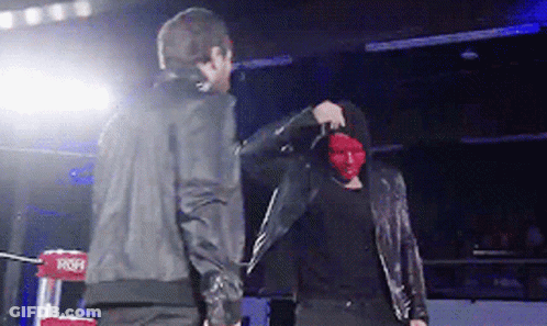 A Man Wearing A Red Mask Stands Next To Another Man In A Black Jacket GIF