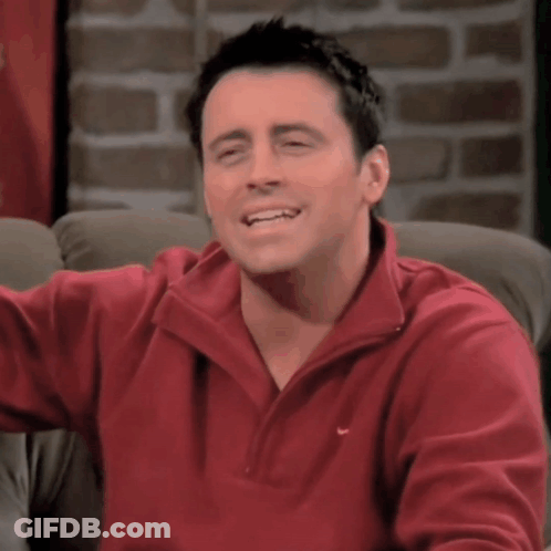 A Man Wearing A Red Nike Sweater Smiles While Sitting On A Couch GIF