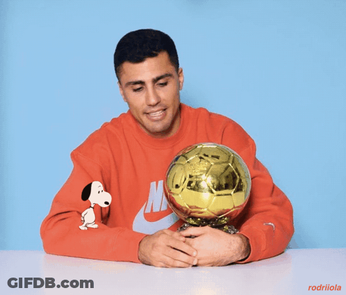 A Man Wearing A Red Nike Sweatshirt Is Holding A Golden Soccer Ball GIF