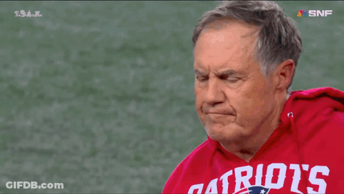 A Man Wearing A Red Patriots Sweatshirt Stands On A Football Field GIF