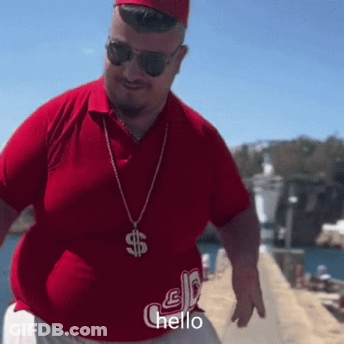 A Man Wearing A Red Shirt And A Dollar Sign Necklace Is Saying Hello GIF