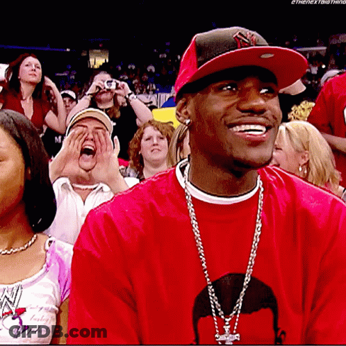 A Man Wearing A Red Shirt And A Ny Hat Is Smiling In A Crowd GIF