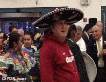 A Man Wearing A Red Shirt And A Sombrero Is Standing In A Crowd . GIF