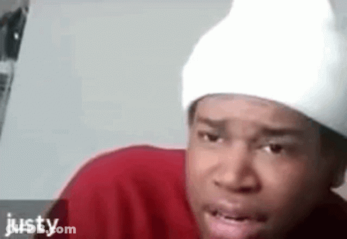 A Man Wearing A Red Shirt And A White Beanie Is Making A Funny Face . GIF