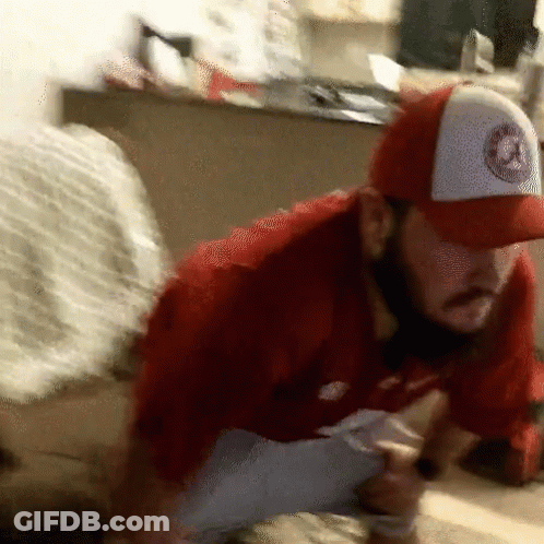 A Man Wearing A Red Shirt And A White Hat With A Logo On It Is Kneeling Down GIF