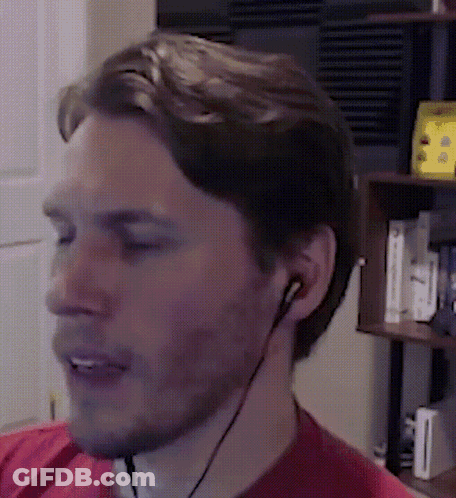 A Man Wearing A Red Shirt And Earbuds Looks At Something GIF