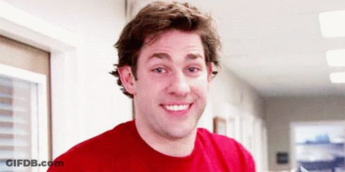 A Man Wearing A Red Shirt Is Smiling In A Hallway GIF
