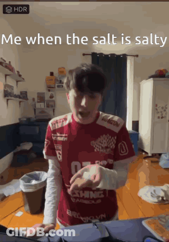 A Man Wearing A Red Shirt That Says " Me When The Salt Is Salty " Is Standing In A Messy Room GIF