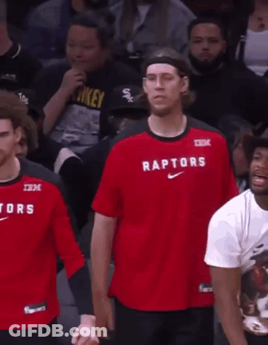 A Man Wearing A Red Shirt That Says Raptors Stands In Front Of A Crowd GIF