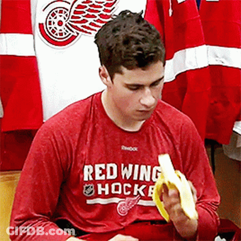 A Man Wearing A Red Shirt That Says Red Wing Hockey Is Eating A Banana GIF