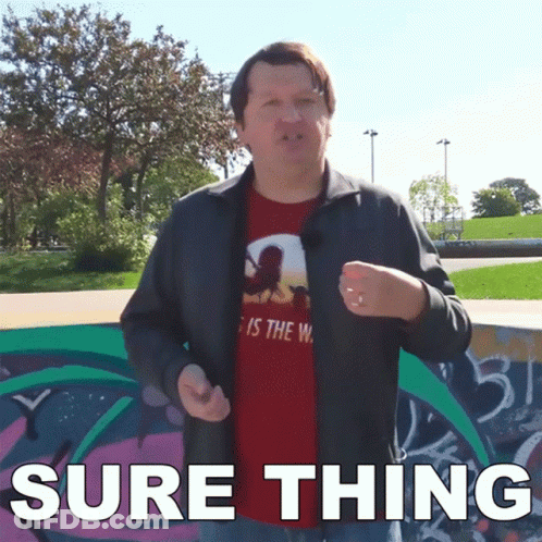 A Man Wearing A Red Shirt That Says " Sure Thing " Stands In Front Of A Graffiti Wall GIF