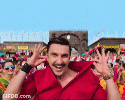 A Man Wearing A Red Shirt With A Mustache Is Smiling In Front Of A Crowd GIF