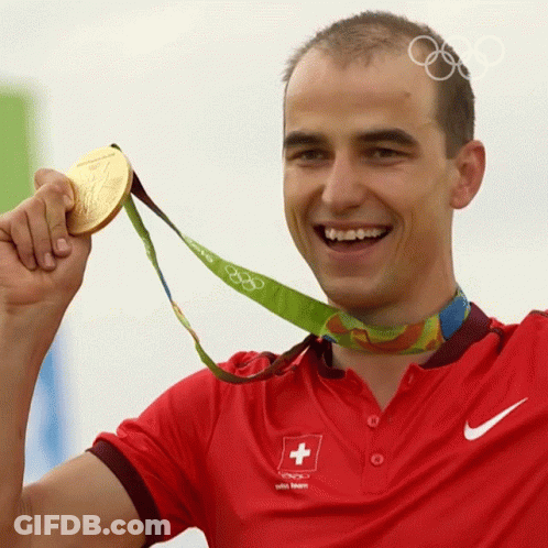 A Man Wearing A Red Shirt With A Swiss Cross On It Holds Up A Gold Medal GIF