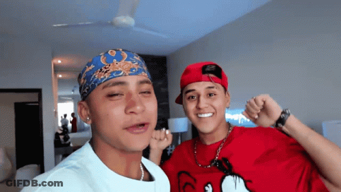 A Man Wearing A Red Shirt With Mickey Mouse On It Stands Next To Another Man Wearing A Bandana GIF