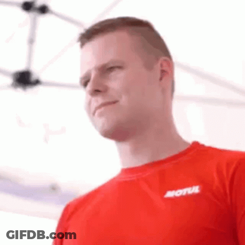 A Man Wearing A Red Shirt With The Word Motul On It Is Standing In Front Of A White Tent . GIF