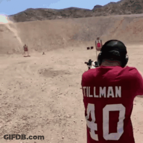 A Man Wearing A Red Shirt With Tillman On The Back Is Shooting A Gun GIF