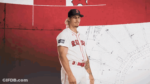 A Man Wearing A Red Sox Jersey Stands In Front Of A Red And White Flag GIF