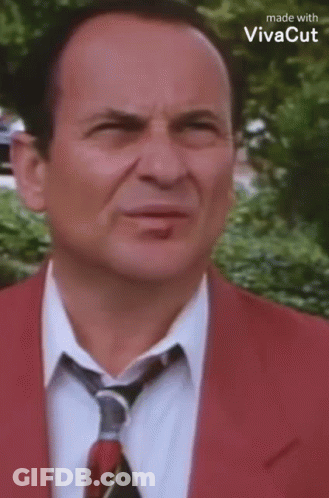 A Man Wearing A Red Suit And Tie Is Making A Funny Face . GIF