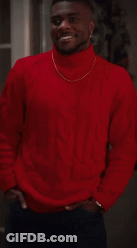 A Man Wearing A Red Sweater And A Gold Chain Around His Neck Smiles GIF