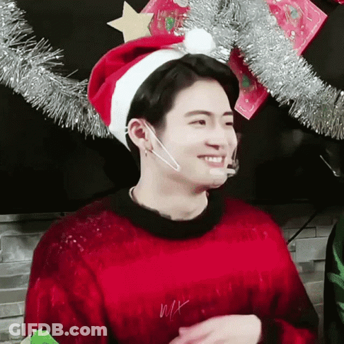 A Man Wearing A Red Sweater And A Santa Hat Is Smiling . GIF