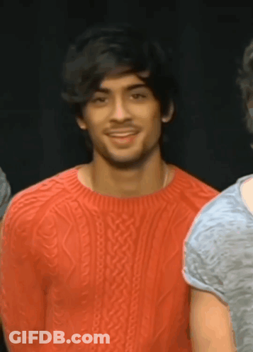 A Man Wearing A Red Sweater Is Smiling And Looking At The Camera GIF