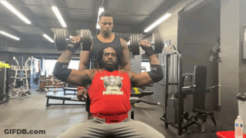 A Man Wearing A Red Tank Top That Says Twist Is Lifting Dumbbells In A Gym GIF