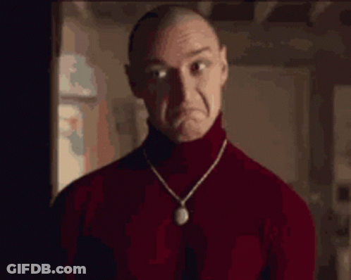 A Man Wearing A Red Turtleneck Sweater And A Necklace Is Making A Sad Face . GIF