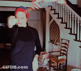 A Man Wearing A Red White And Blue Beanie Is Standing In Front Of A Staircase GIF
