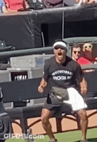 A Man Wearing A Rogue T-Shirt Is Sitting On A Bench On A Baseball Field . GIF